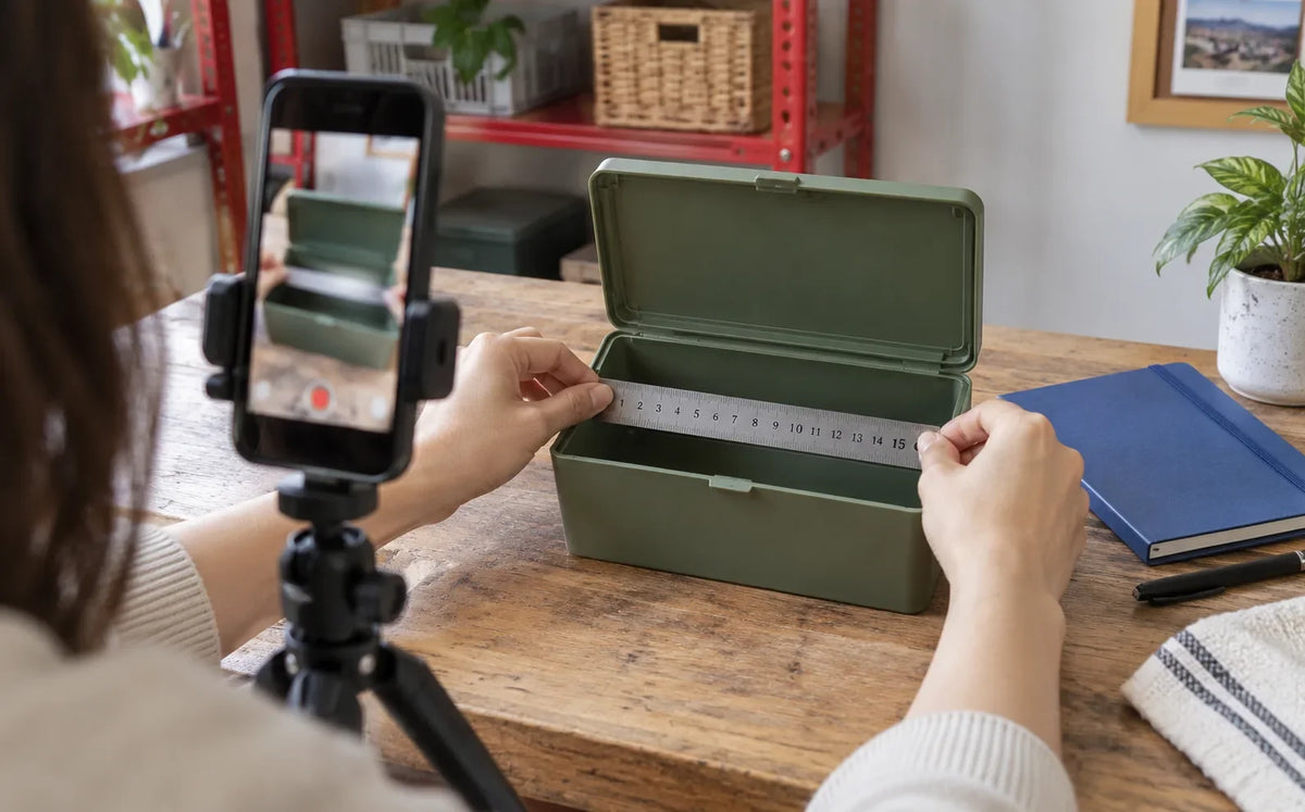 A creator films the interior measurement of a green storage box with a phone on a tripod.